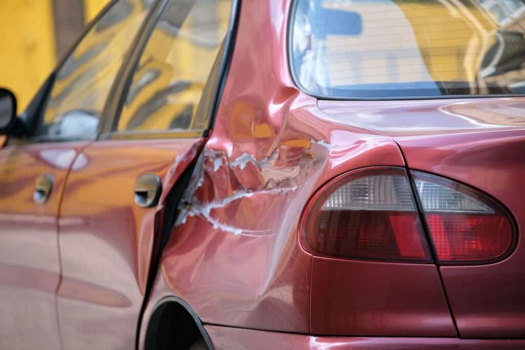 Dented car with damaged body parked on city street side.